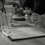 Close-up of hands writing notes in an office setting with drinks on a table.